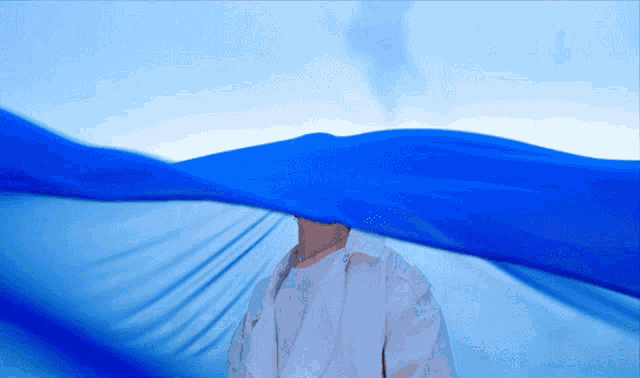 a man in a white shirt is covering his face with a large blue cloth