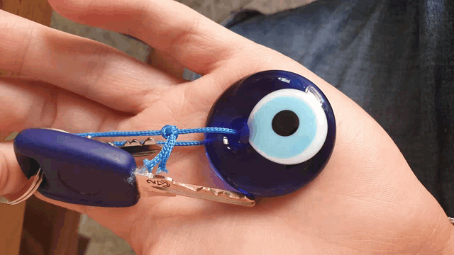 a person is holding a keychain with a blue evil eye