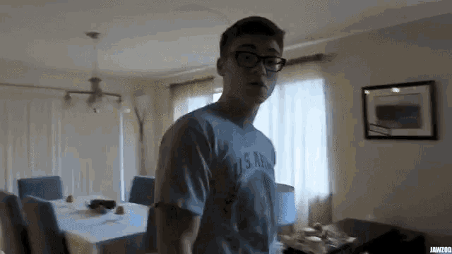 a young man wearing a us navy shirt stands in a living room
