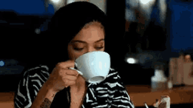 a woman is drinking a cup of coffee from a white cup .