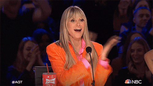 a woman in an orange jacket is standing in front of a microphone with a sonic drink next to her