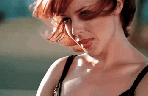 a woman with red hair and a black bra looks at the camera