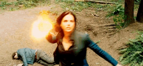a woman is holding a fireball in her hand and a man is laying on the ground behind her