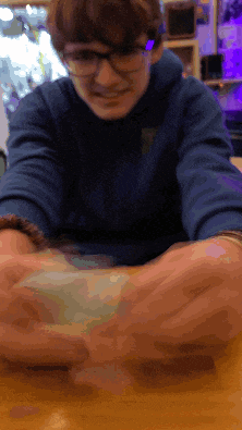 a man wearing glasses is sitting at a table with his hands outstretched