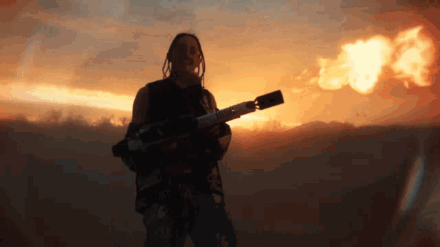 a man with dreadlocks is holding a rocket in front of a sunset