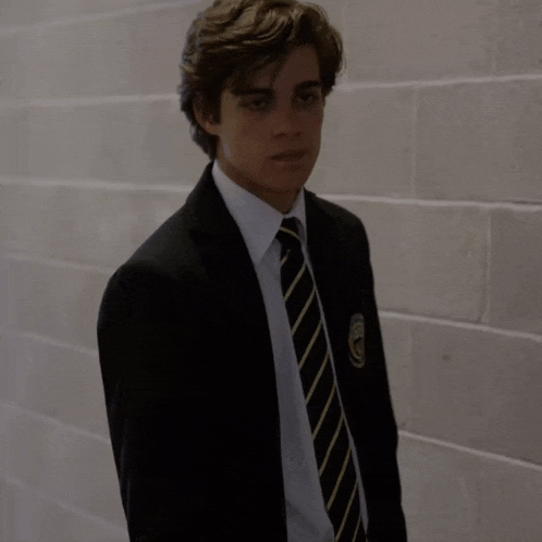 a young man in a suit and tie is standing in front of a white brick wall