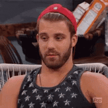 a man with a beard wearing a red hat and a tank top with stars .