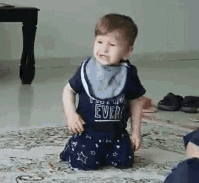 a baby is kneeling on the floor with a bib on .