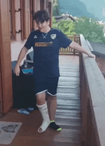a boy wearing a rossi t-shirt and shorts is standing on a balcony