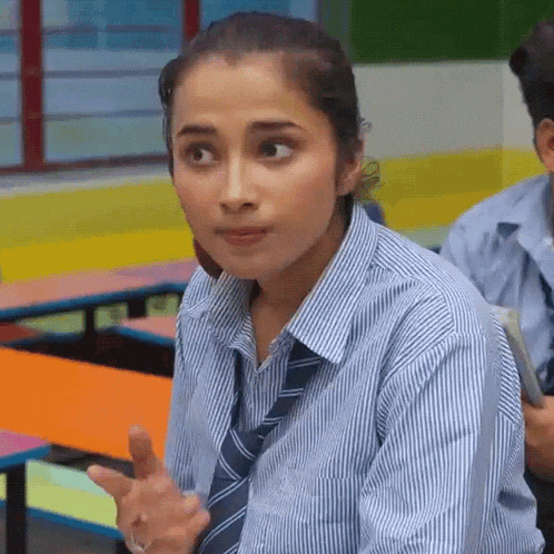 a girl in a striped shirt and tie is sitting in a classroom with other students .