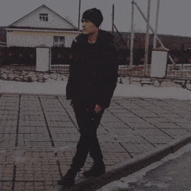 a man wearing a black jacket and black pants is walking down a sidewalk with umarov written on the side of his pants