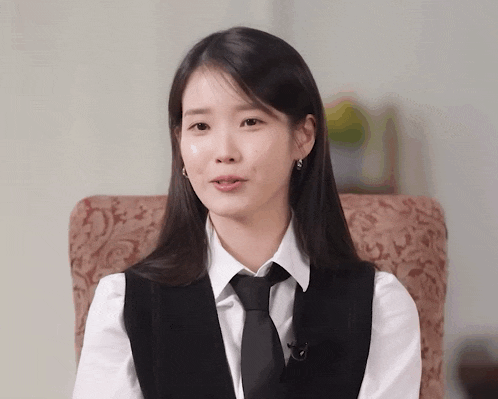 a woman wearing a vest and tie is sitting on a chair