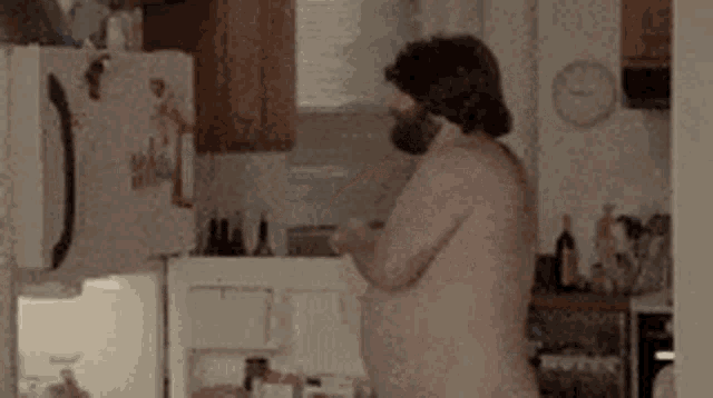 a naked man with a beard is standing in a kitchen with a clock on the wall .