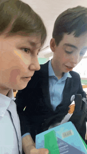 two boys are in a classroom and one of them is holding a book with a label that says ' russian ' on it
