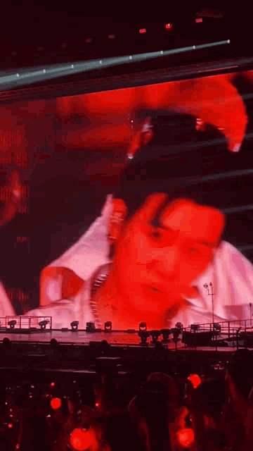 a man 's face is projected on a large screen in a crowded room