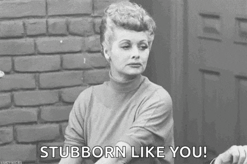a black and white photo of a woman sitting in front of a brick wall saying `` stubborn like you '' .