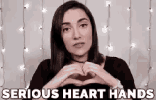 a woman is making a heart shape with her hands and the words `` serious heart hands '' behind her .