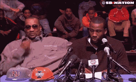 two men are sitting at a table with microphones and one has a hat that says ku on it