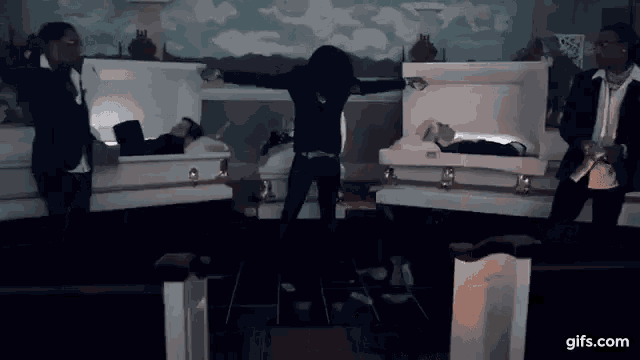 a group of people are standing in front of coffins with a man laying in one of them .