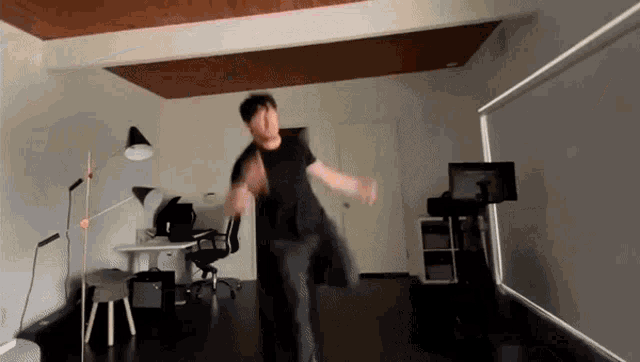 a man in a black shirt is dancing in a room with a desk and chair