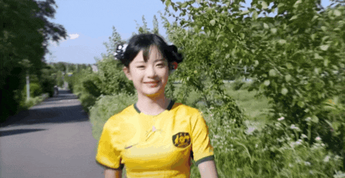 a young girl wearing a yellow nike jersey is walking down a path .