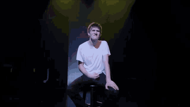 a man in a white t-shirt is sitting on a stage