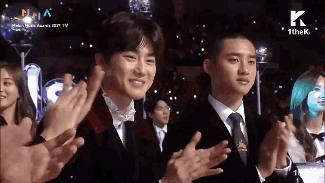 a man in a suit and tie applauds at a music awards