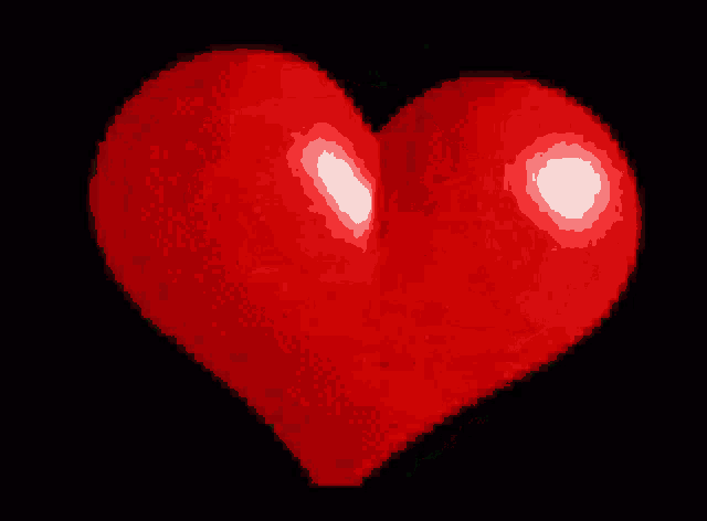 a red heart is glowing in the dark with a black background