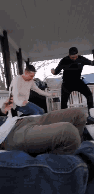 a group of men are dancing on a porch and one of them is holding a cell phone