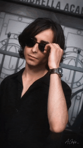 a man wearing sunglasses and a watch is standing in front of a building that says umbrella academy