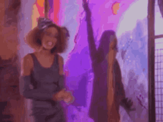 two women are dancing in a room with purple lights behind them