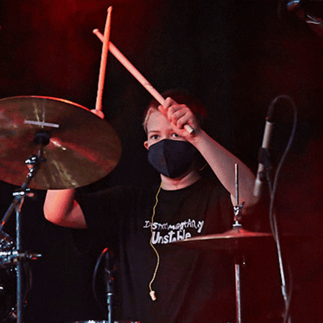 a young man wearing a black shirt that says instrumentary unstable playing drums