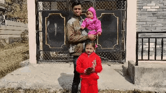 a man is holding two children in his arms in front of a gate .