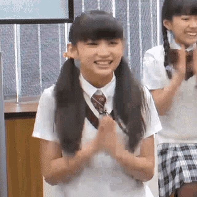 a girl in a white shirt and tie is smiling and clapping her hands