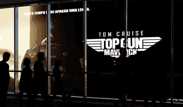 a silhouette of people walking in front of a window with a tom cruise top gun maverick poster