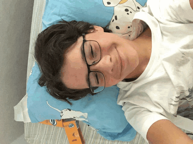 a young boy wearing glasses laying on a bed with a dalmatian pillow