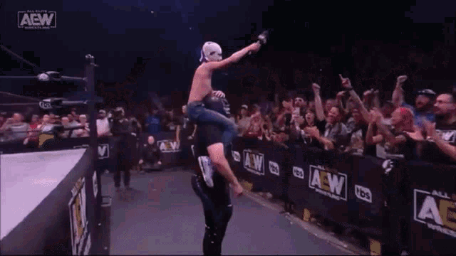 a wrestler is being lifted in the air by another wrestler in front of a crowd that is cheering .
