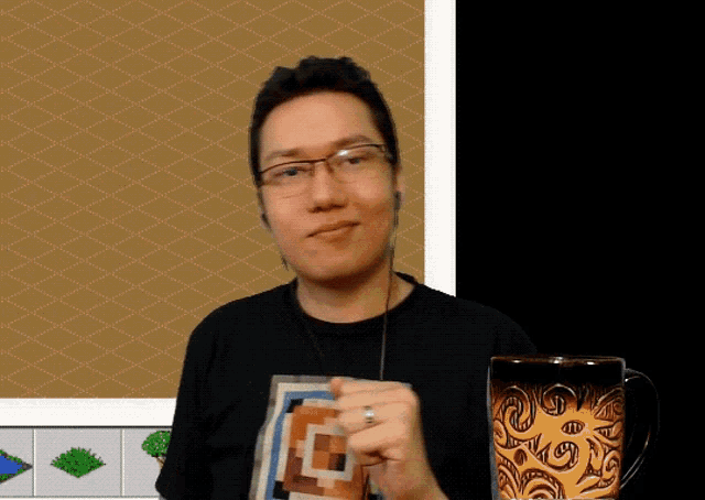a man wearing glasses and a black shirt with the letter e on it holds a mug