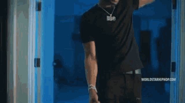 a man in a black shirt is standing in front of a blue door and pointing at something .