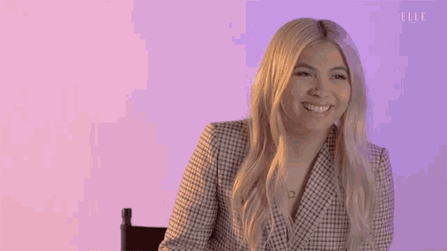 a woman is smiling while sitting in a chair in front of a purple wall .
