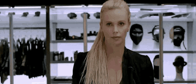 a woman in a black jacket is standing in front of a display case filled with clothes and masks .