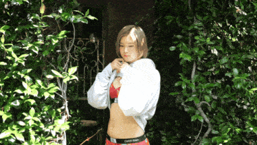 a woman wearing calvin klein underwear is standing in front of a bush