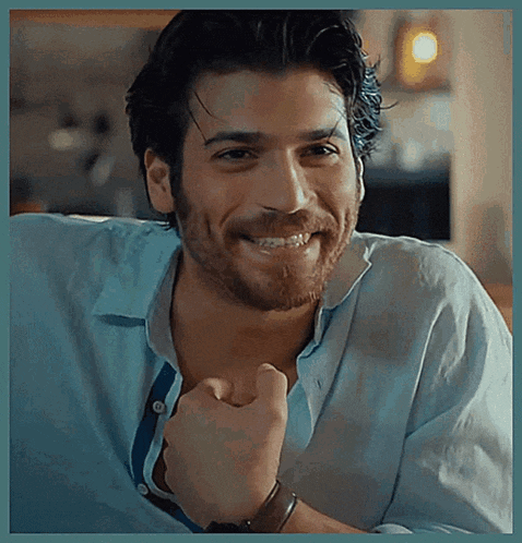 a man with a beard and a blue shirt is smiling and making a fist .