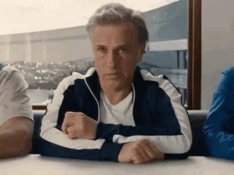 a man in a blue and white track jacket is sitting at a table with his hands folded .