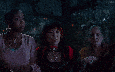 three women are standing in a dark forest and one of them is asking if she is a green witch
