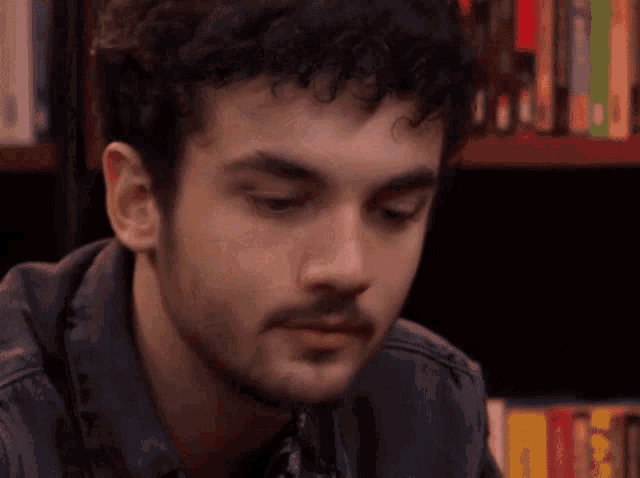 a close up of a man 's face in front of a bookshelf