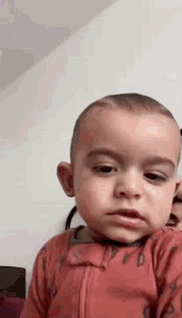 a baby in a red outfit is making a funny face while looking at the camera .