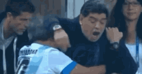 a man in a blue and white shirt is hugging another man in a black jacket .
