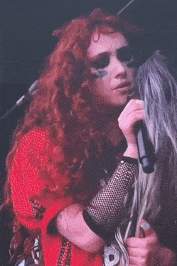a woman with red hair is singing into a microphone while another woman with blonde hair is looking at her .