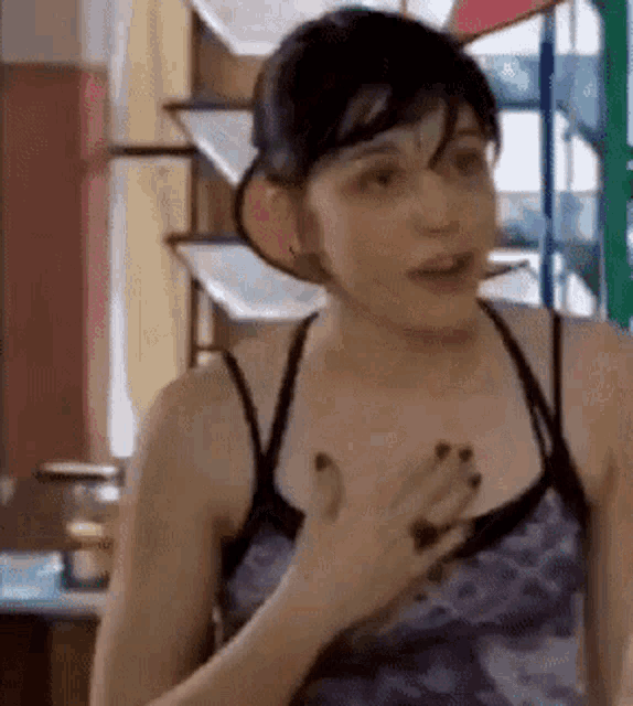 a woman in a blue tank top is holding her chest and looking at the camera .